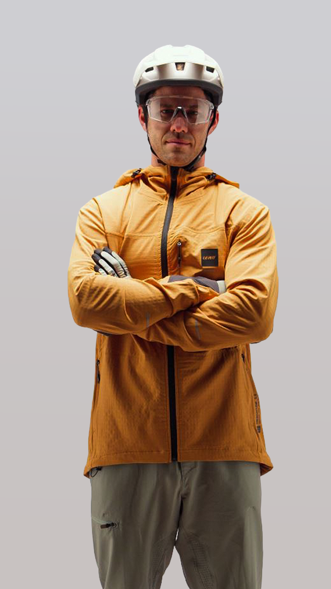 Person wearing a mustard yellow jacket and helmet with arms crossed on a gray background
